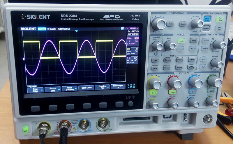 A bench oscilloscope showing a sine wave and offset square wave simultaneously. Image © Wild Pancake/CC-BY-4.0.